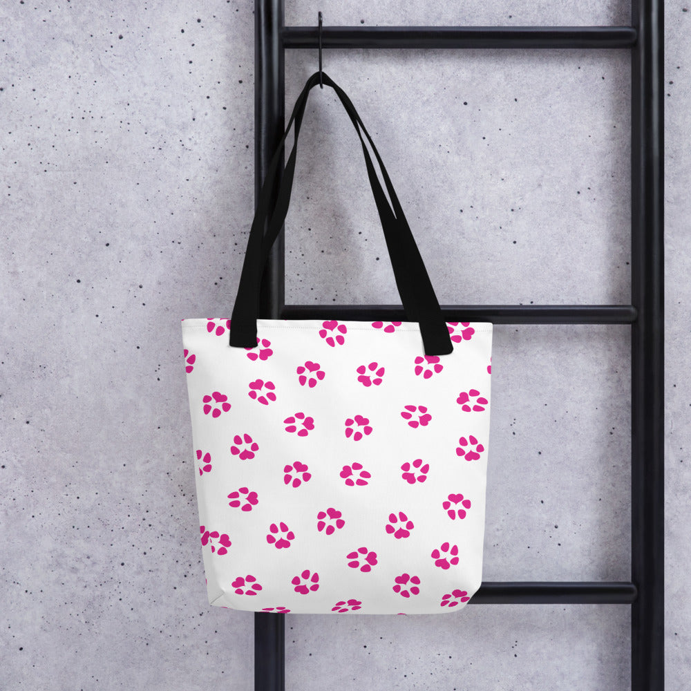 Tote bag with white background and black handle. This is the back. Dog paw prints all over in pink.