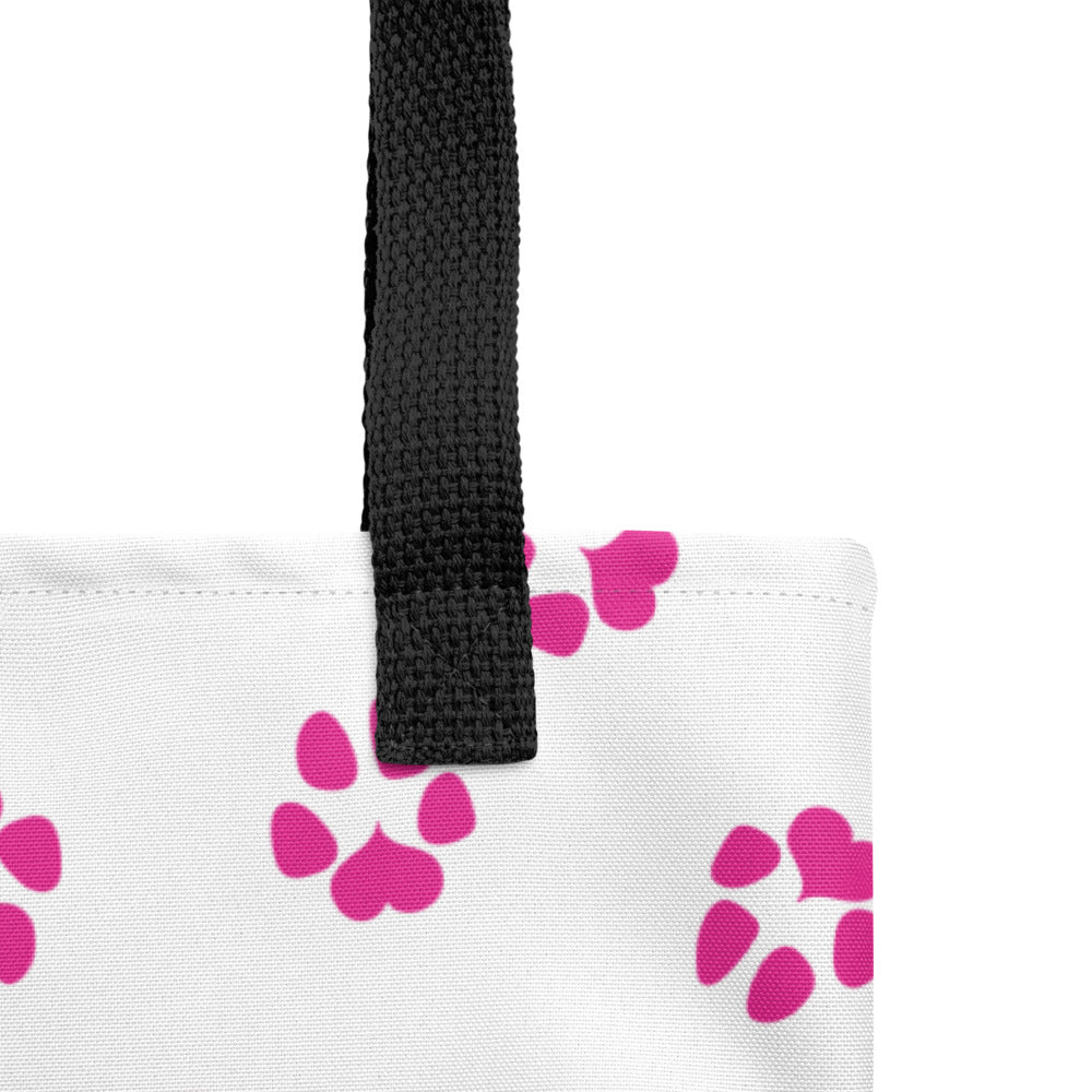 Close up of tote bag with white background, pink dog paw prints and black handle.