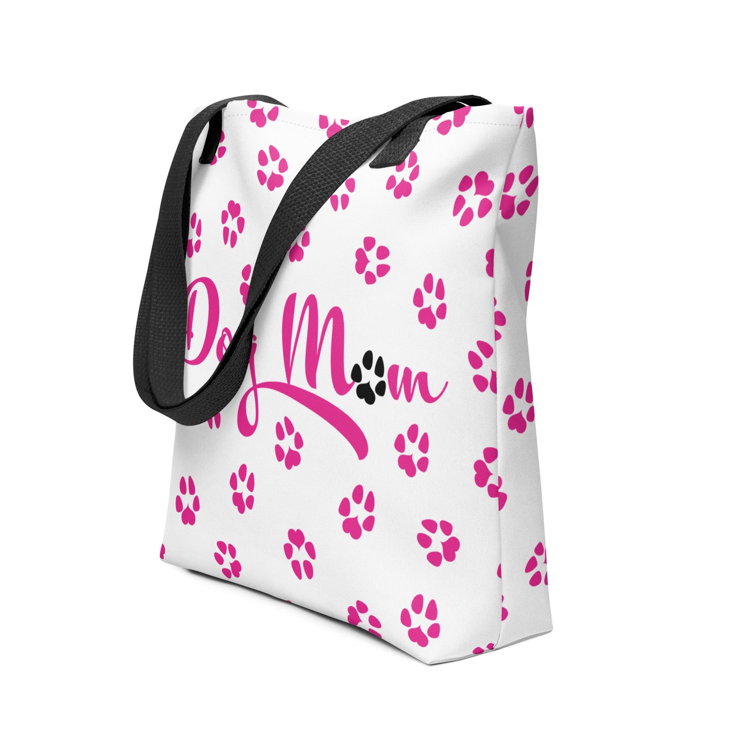 Tote bag with white background and black handle. Dog Mom is written on the front with dog paw prints all over in pink with one black paw in Mom.