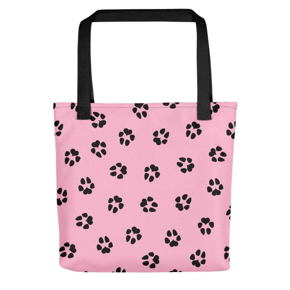 Tote bag with pink background. The back side of the bag is shown with dog paw prints all over in black. The handle is black