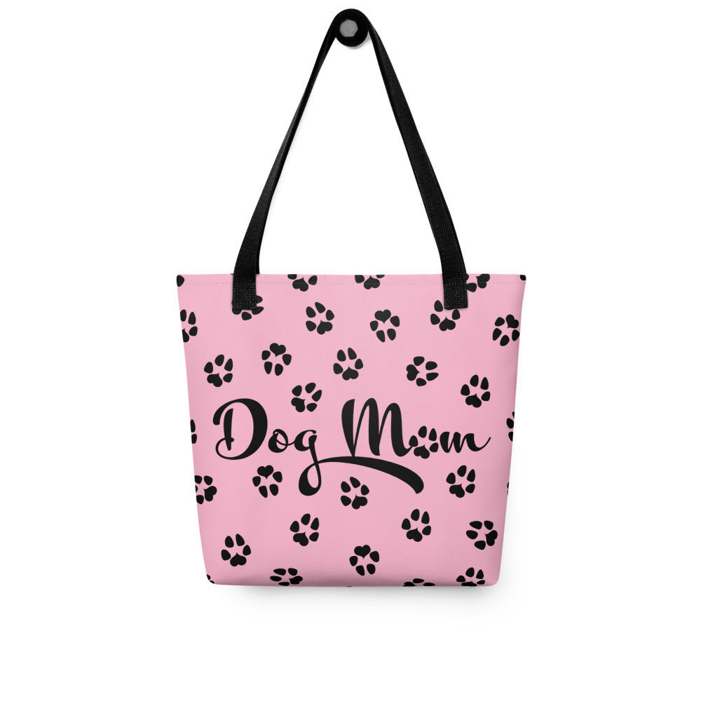 Tote bag with pink background. Dog Mom is written on the front with dog paw prints all over in black. The handle is black