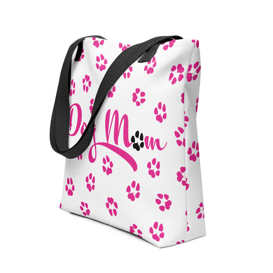 Tote bag with white background and black handle. Dog Mom is written on the front with dog paw prints all over in pink with one black paw in Mom.